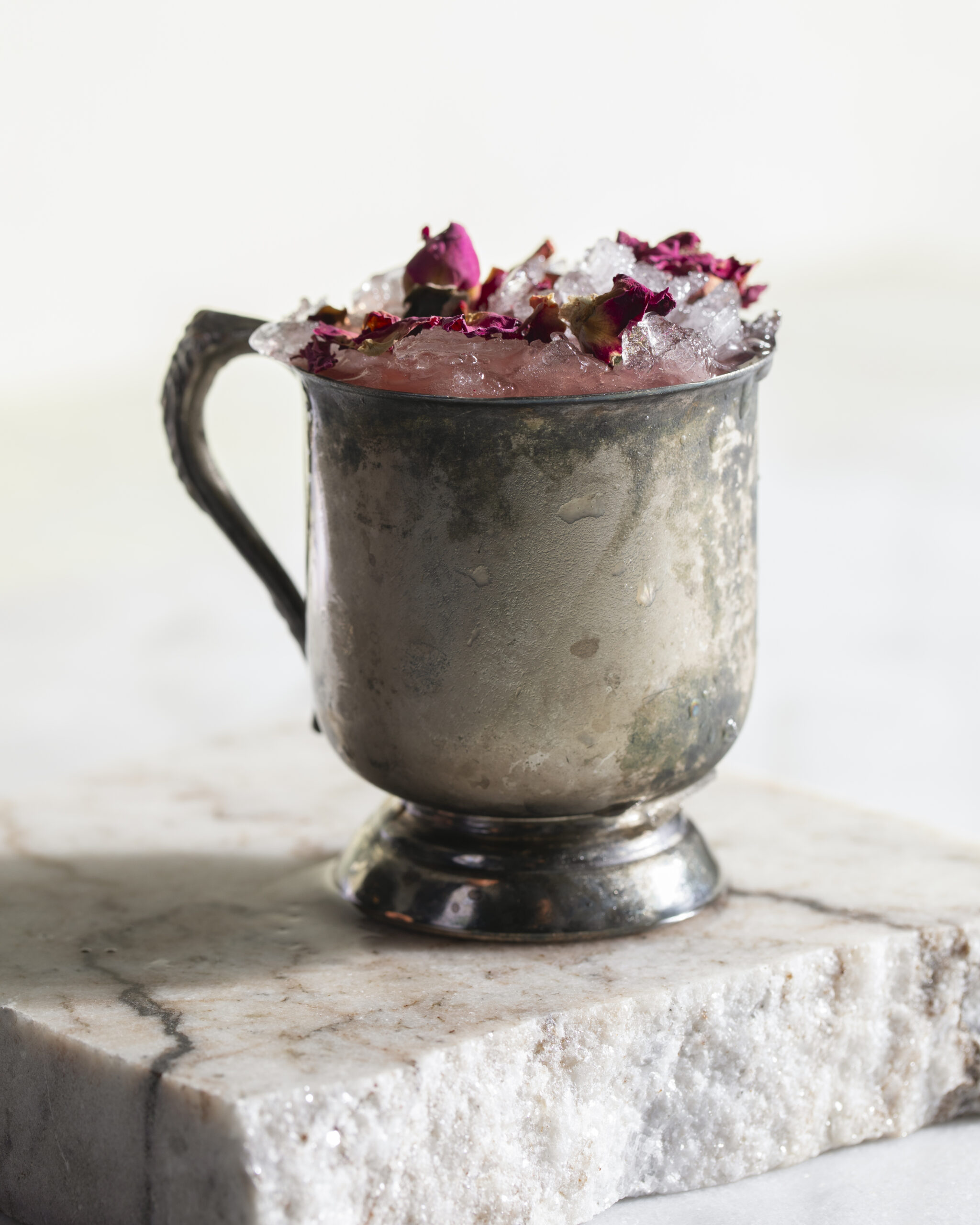 A pink Parfait Amour Gulab cocktail sits in a silver mug.