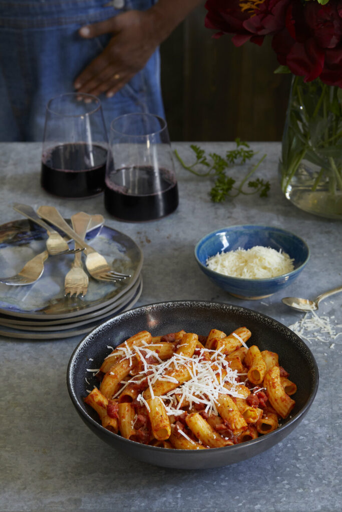 Stanley Tucci Inspired Pasta alla Norma sits in a bowl to the right with two glasses of red wine off to the back left.