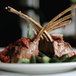 Rack of lamb sits on a white plate.