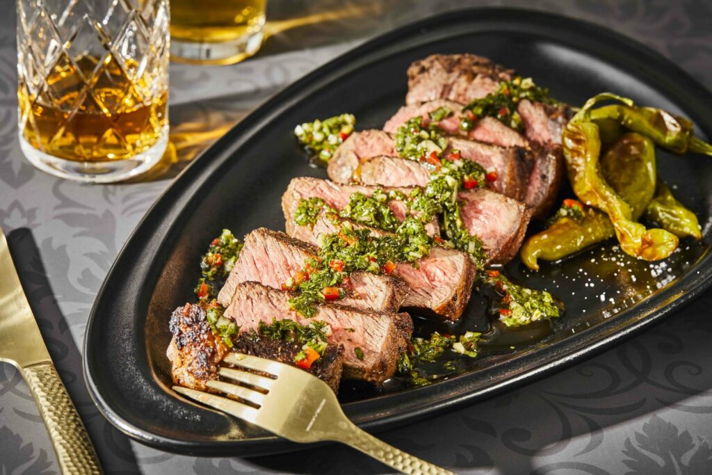 a sliced new york strip steak with green chimichurri on a black plate