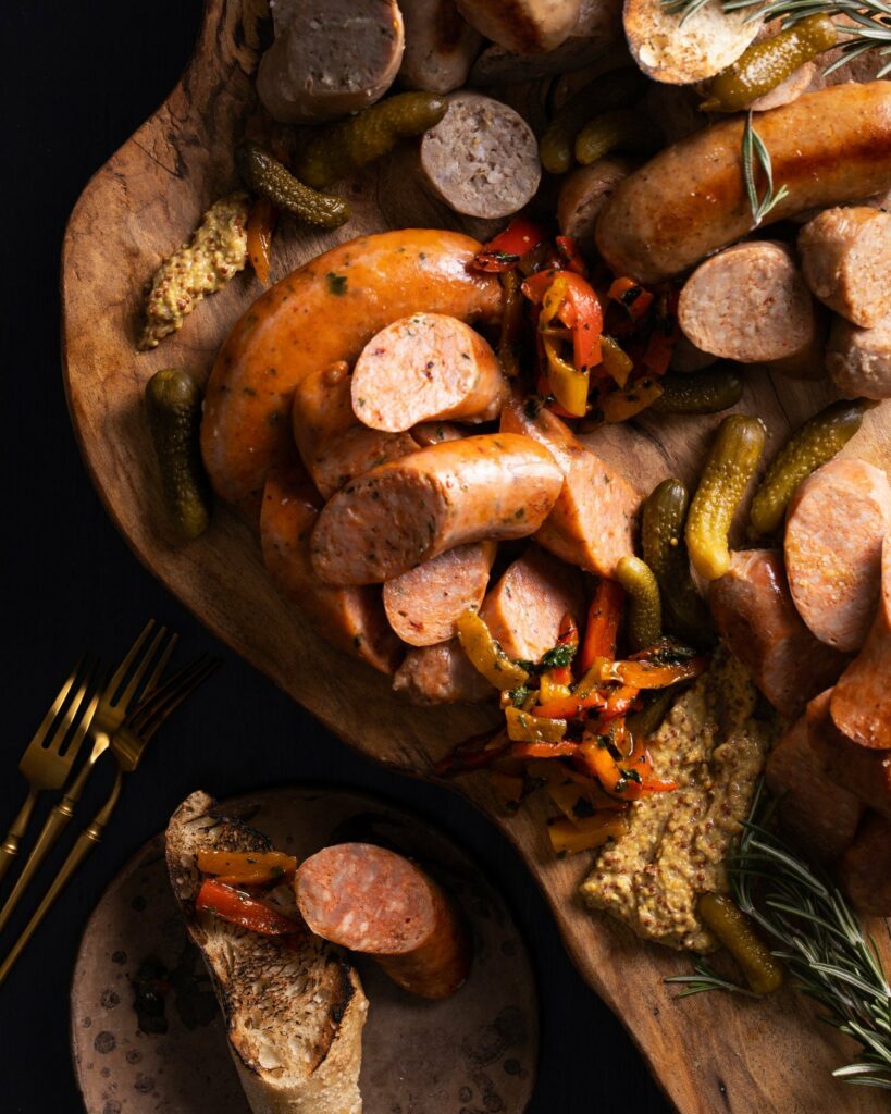 A variety of sliced sausage on a wooden board with mustard for dipping. Tailgating Recipes