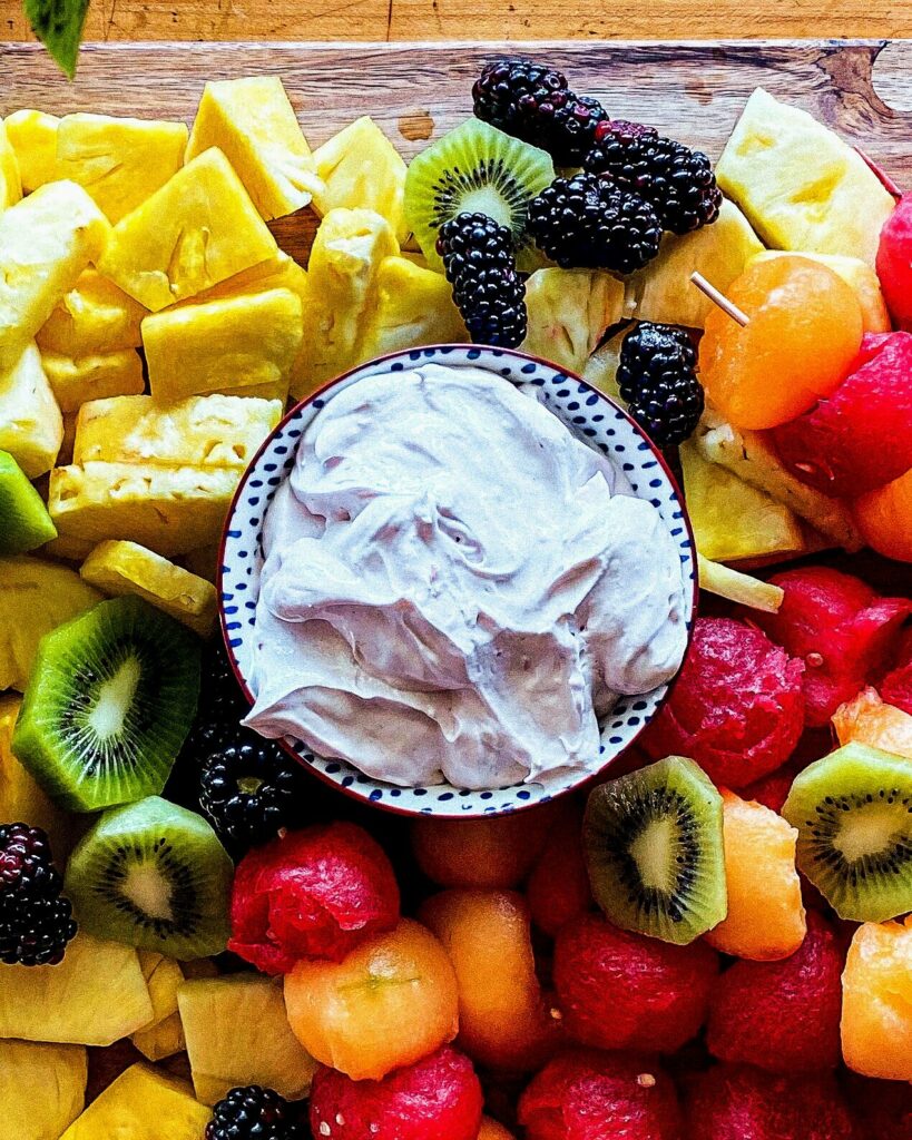 Fruit Dip in a small bowl surrounded by various fruits including pineapple, raspberries, kiwi, and more.