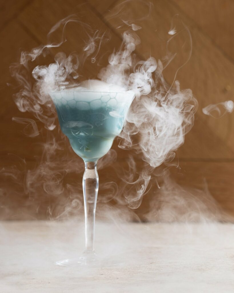 A Tiffany Blue colored winter cocktail called Snow Miser, in a Nick and Nora glass with dry ice.l