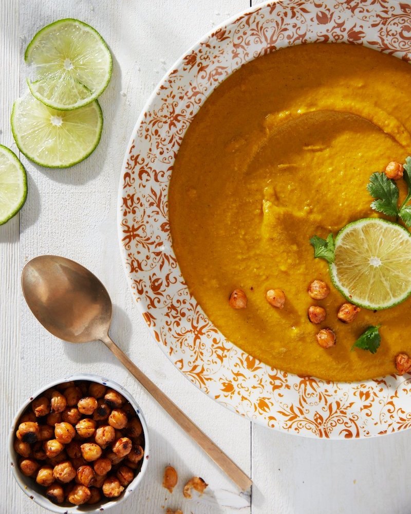 Allergen-free Golden Soup in a plate; a spoon, pieces of lemon, and chickpeas on the side.