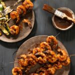 Apple Butter BBQ Sauce in a small bowl with a brush placed on it. Shrimp on sticks with bbq sauce on them.