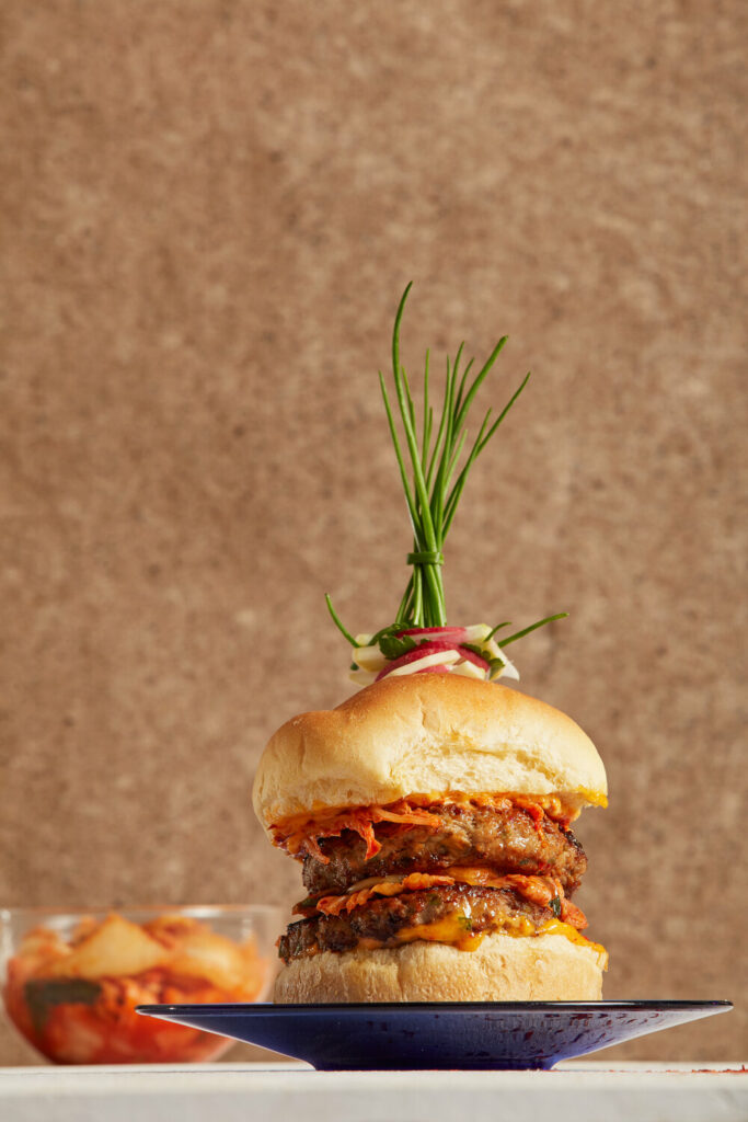 a thick double burger made of lamb with a fancy herb garnish on top on a black plate with a brown background