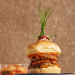 a thick double burger made of lamb with a fancy herb garnish on top on a black plate with a brown background