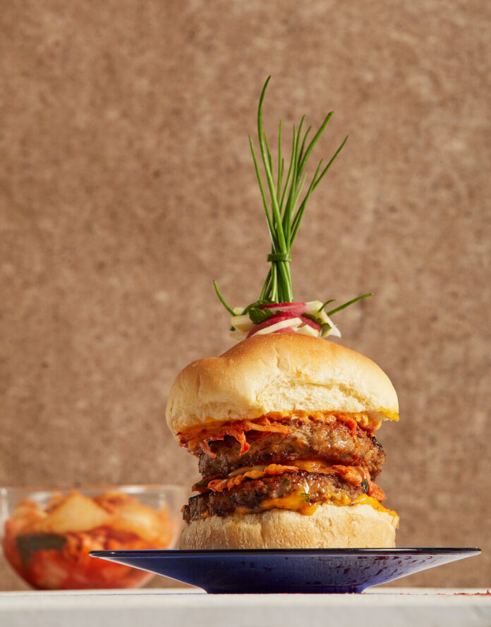 a thick double burger made of lamb with a fancy herb garnish on top on a black plate with a brown background