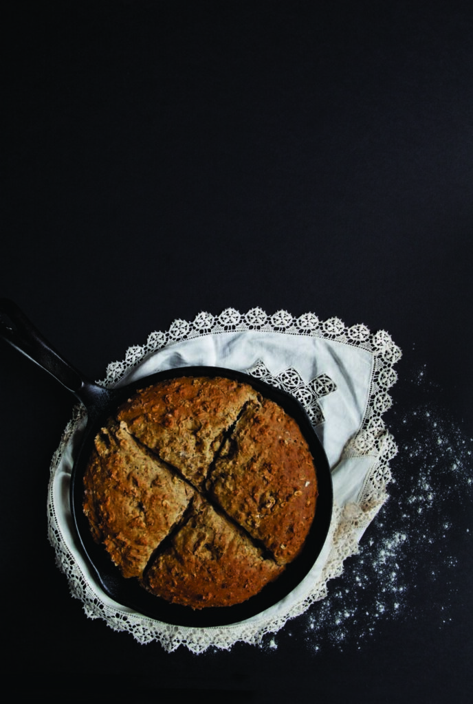 Buttermilk Soda Bread with Fennel Pollen in a frying pan placed on a napkin, which is placed on a dark black surface with sprinkled flour on it