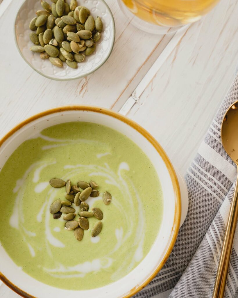 Caramelized fennel soup in a bowl on a white wooden surface with a spoon and a small bowl of toppings on the side