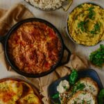 Chicken Chaap on a frying pan with several side dishes on the sides