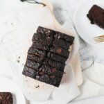 Chocolate Zucchini Bread cut into small pieces on a wooden serving tray. The corners show two plates cut in half with a small piece of bread on each