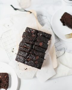 Chocolate Zucchini Bread cut into small pieces on a wooden serving tray. The corners show two plates cut in half with a small piece of bread on each