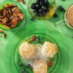 three Coconut Macaroons on a glass plate on a green surface. Walnuts and berries in separate small bowls