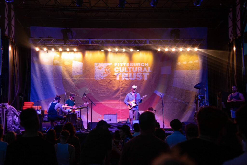 An image of a singer playing guitar onstage at the Three Rivers Arts Festival.