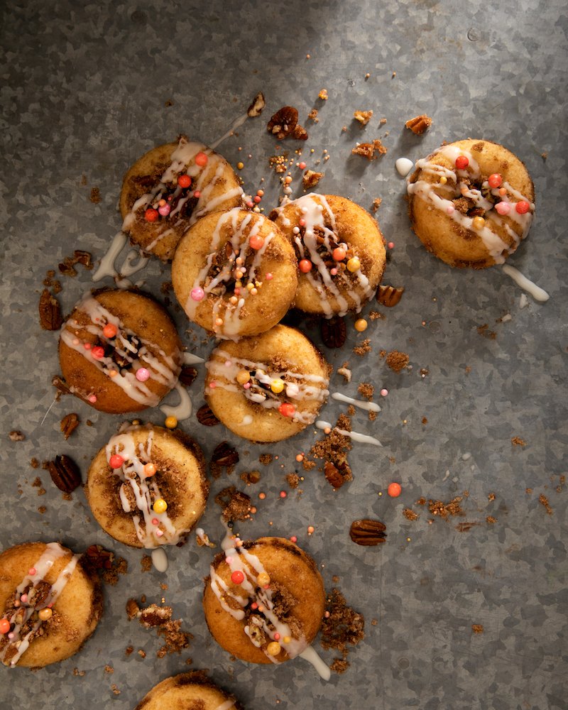 9 Crumb Cake Donuts placed across a table with crumbs and sauce