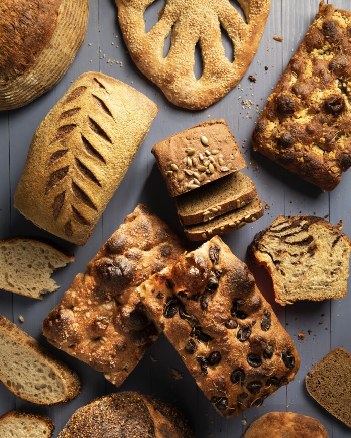 a variety of bread types both whole loaves and sliced on a blue grey wooden background from Crust Worthy