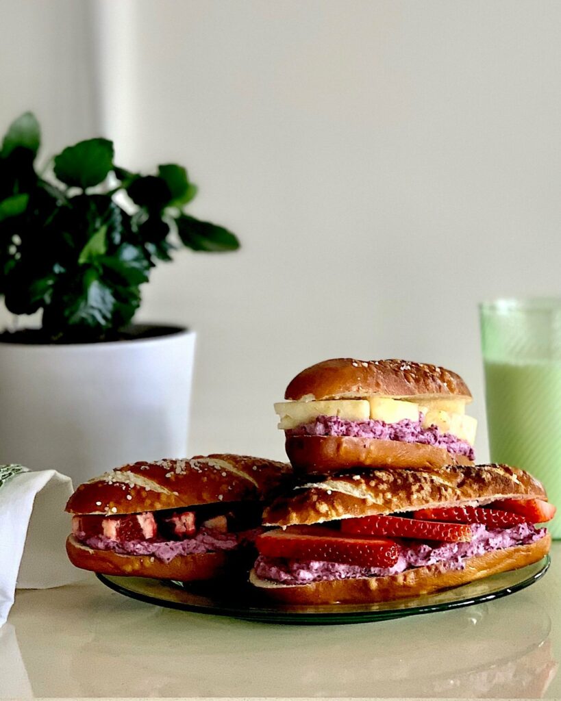 Three fresh fruit and Creme Cheese Sammies sit stacked on a plate next to a glass filled with green liquid.