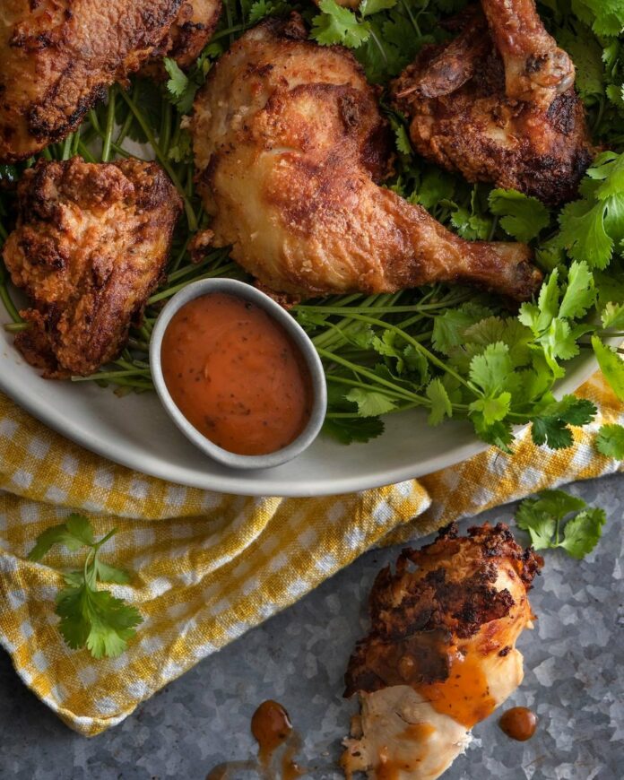 A white plate topped with chicken wings next to a bowl of sauce.