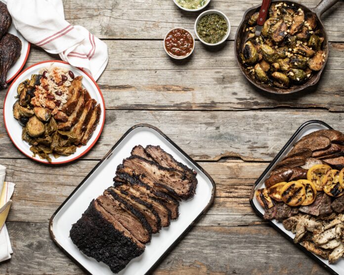 four different dishes of meat and vegetable served family style on a wooden table