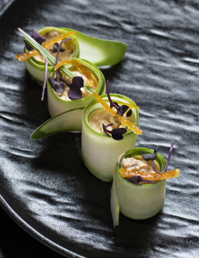 Cucumber rolls in a line on a pattern dish.