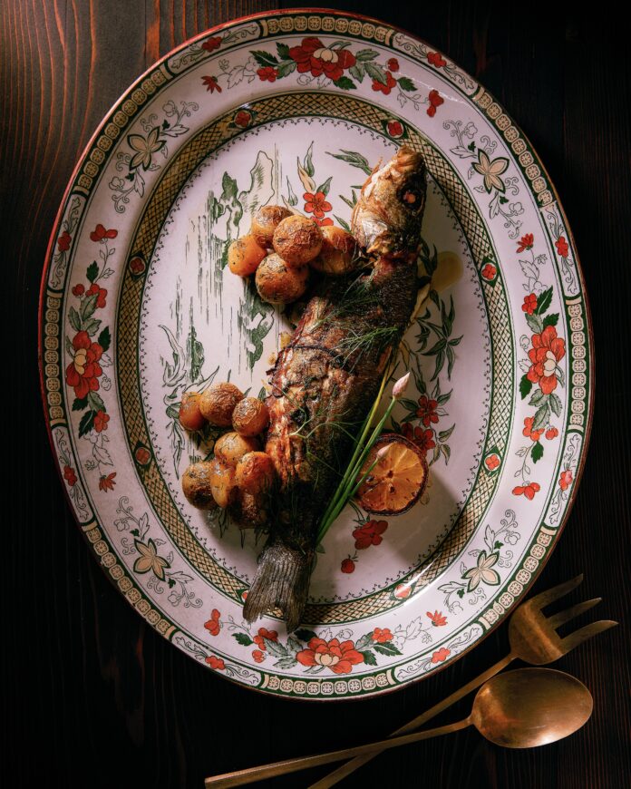 a whole trout with roasted new potatoes and lemon garnish on an oval platter. seafood