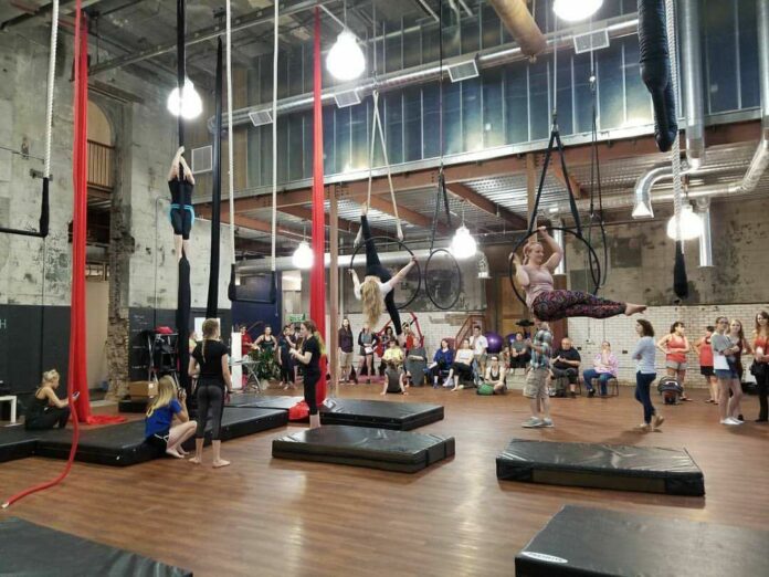 A photo of various people in a gymnasium practicing circus arts.