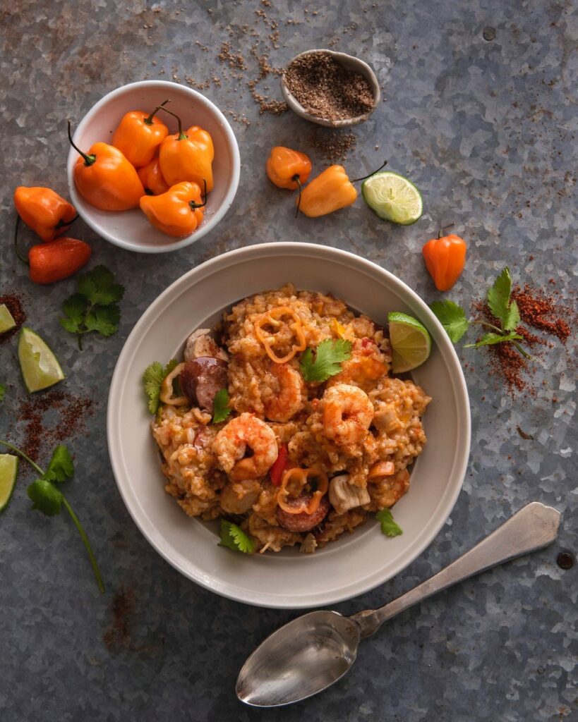 Jambalaya in a bowl placed on a ceramic surface along with a spoon, spices, and lemon
