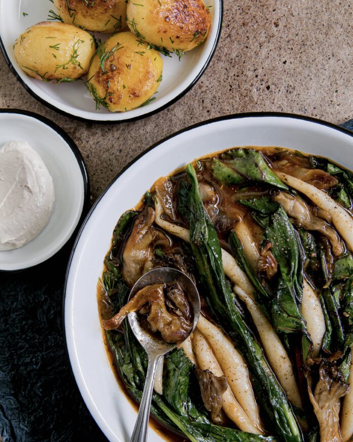 A bowl of iwaki potato dumplings with dill and mushrooms soup in a white bowl on a table with a side bowl of roasted potatoes