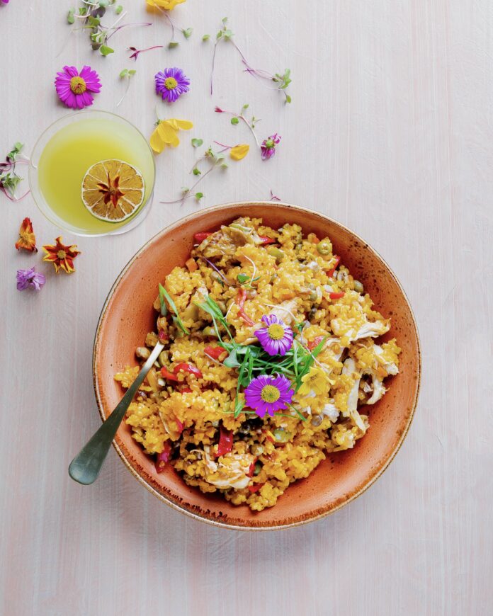 a large terra cotta bowl filled with a rice dish decorated with edible flowers, a delicious latin food