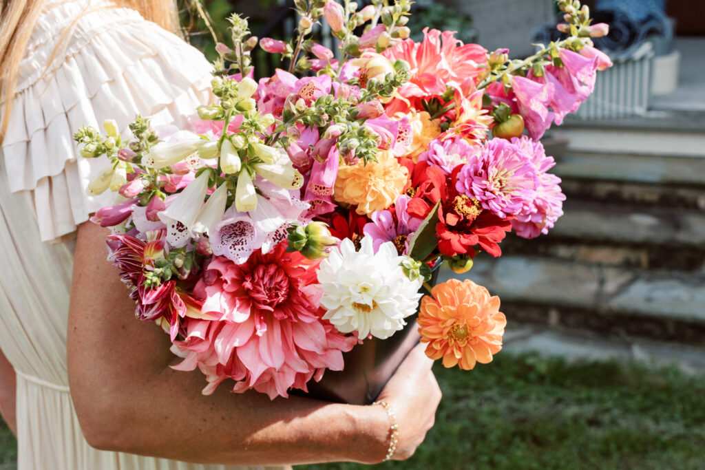 a woman in a white dress on with an armful of pastel colored Dalias and zinnias