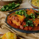 Macher Jhol (Bengali Fish Curry) served in a partially visible skillet along with side salad and rice