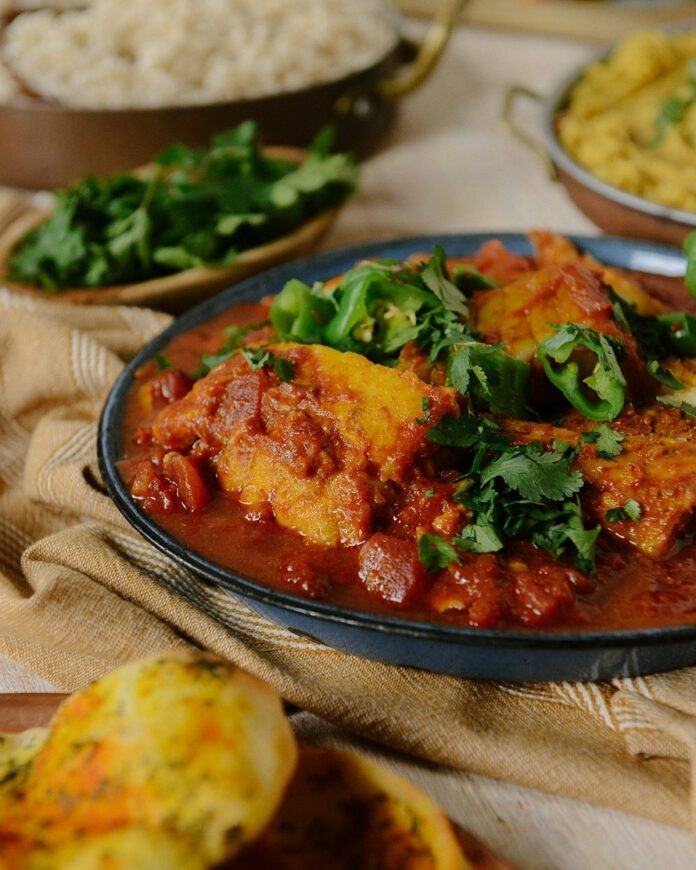 Macher Jhol (Bengali Fish Curry) served in a partially visible skillet along with side salad and rice