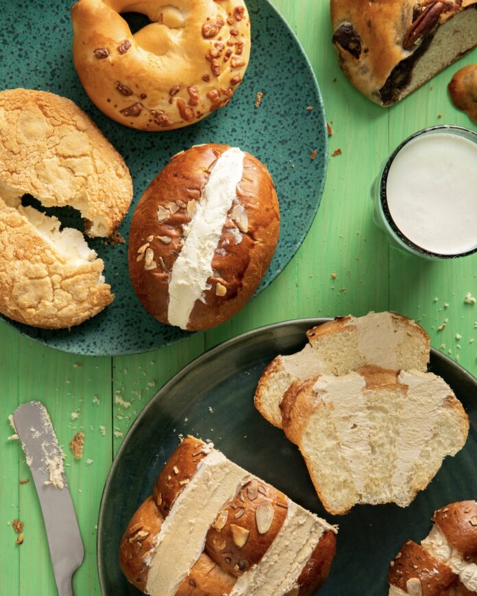 arial photo of sliced sweet bread and buns on plates with a glass of milk on a green background