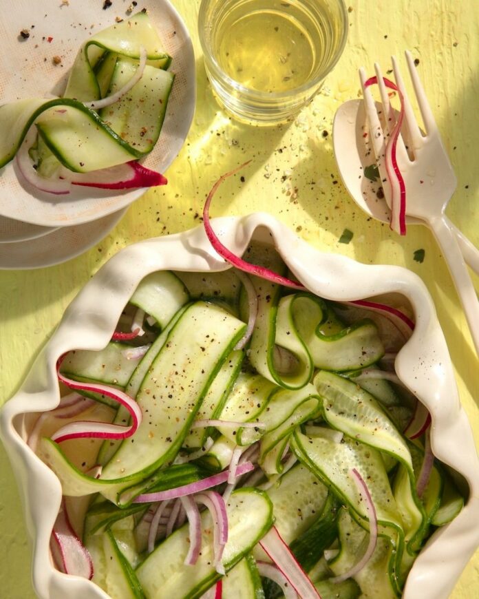 Nana’s Cucumber Salad a bowl filled with Nana’s Cucumber Salad next to a smaller bowl and a fork and a knife