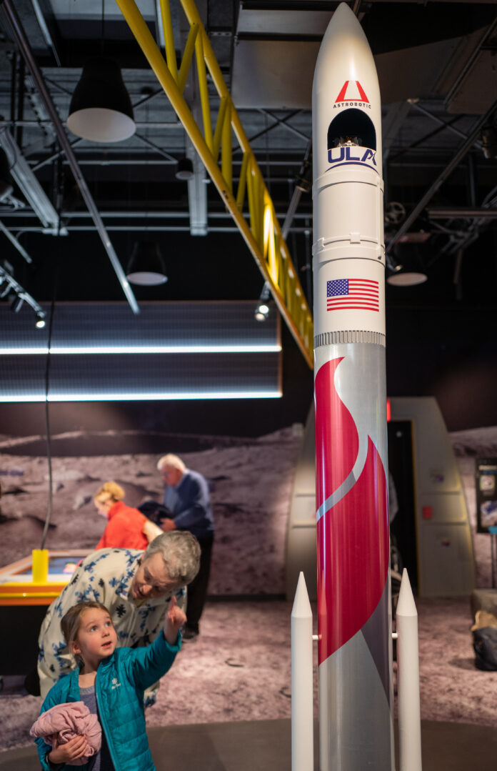 Moonshot Museum, a child stands next to a rocket and smiles while pointing up