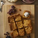 Pumpkin Gooey Butter Cake cut into 9 pieces served on a wooden with grapes and butter as toppings