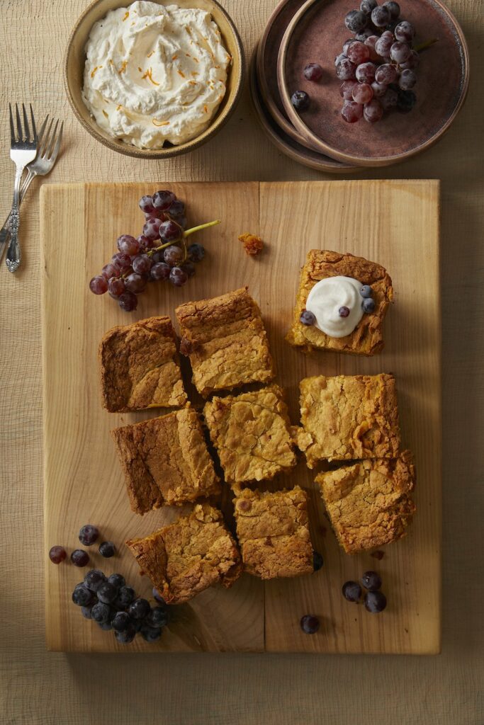 Pumpkin Gooey Butter Cake cut into 9 pieces served on a wooden with grapes and butter as toppings