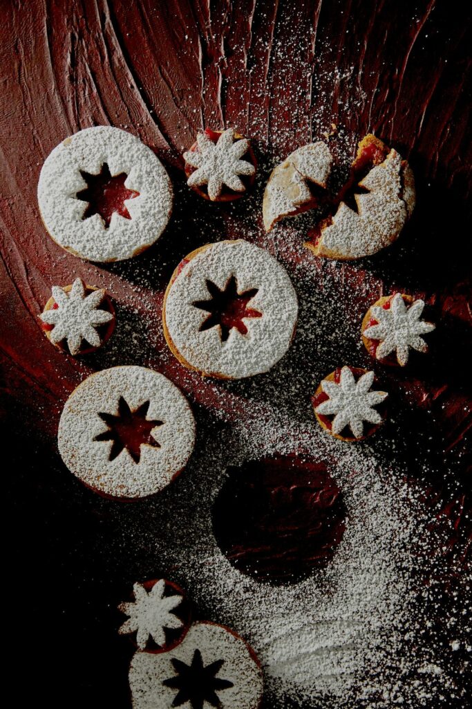 Pumpkin Pie Spice Linzer Cookies spread on a wooden surface, dusted with powdered sugar