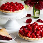 Raspberry Glaze Pie on two different plates along with flowers in a glass of water and a sandwich in a small plate