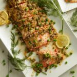 Salmon with Dill Butter Sauce and English Peas served on a white tray with herbs and lemons