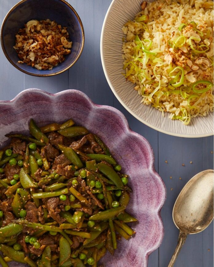 Spring Beef Stir Fry in a purple bowl cut in half. Another bowl of rice cut in half, a half-cut spoon, and a smaller bowl with a side dish.