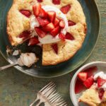 A strawberry cake in a green plate with whipped cream on top and forks on the side