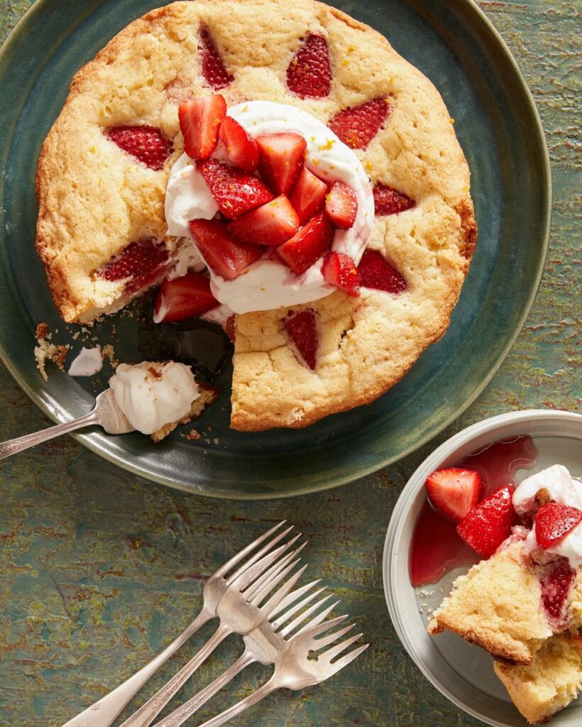 A strawberry cake in a green plate with whipped cream on top and forks on the side