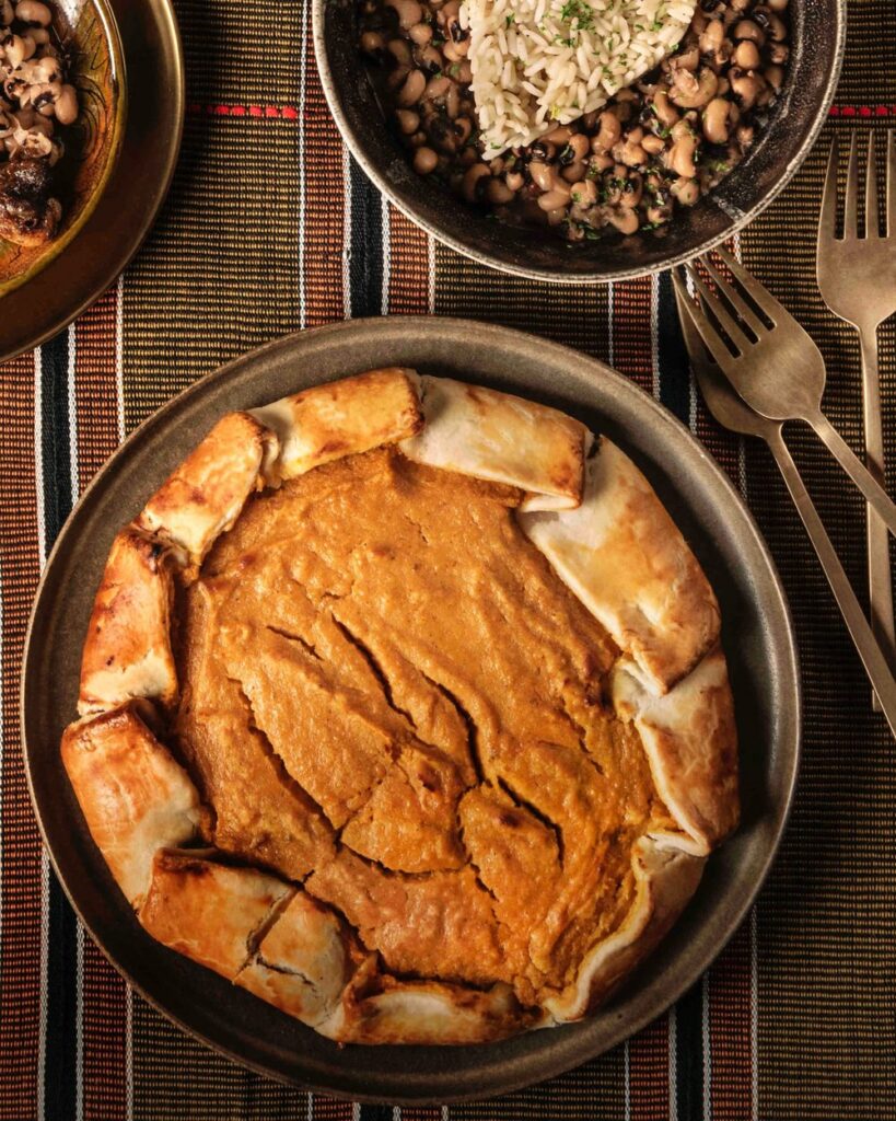 Sweet potato pie served in a metallic plate with three forks and a bowl of black eyed peas on the side