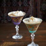 Two Espresso Whiskey Martini fills one purple and one blue martini glasses, adorned with gold accents.