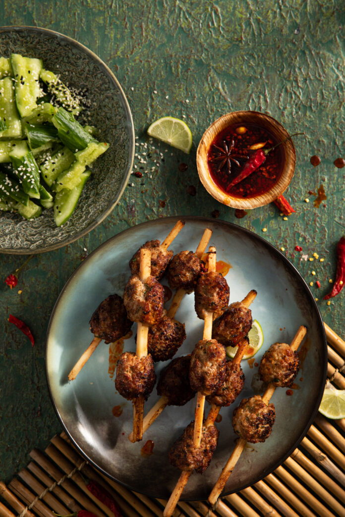 A flat-lay image of Thai Pork Meatball Skewers with limes for garnish and topping.