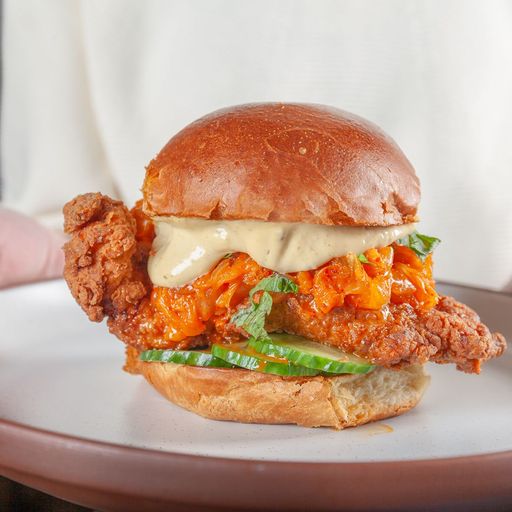 a fried chicken sandwich with white cheese and lettuce and pickles on a white plate