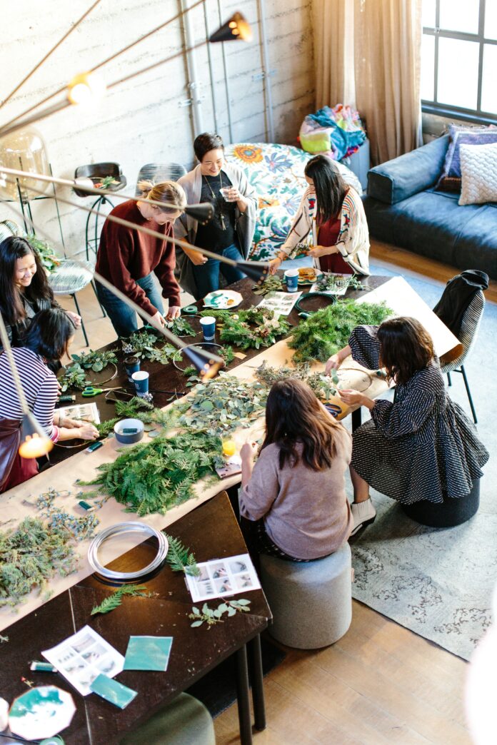 Six women stand and sit around a table using flowers in a workshop. Pittsburgh Workshops