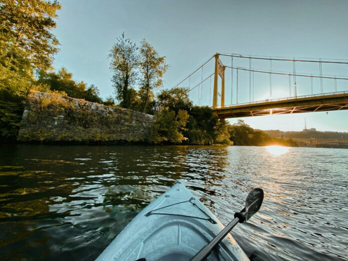 The tip of kayak is shown sitting on the Monongahela River, looking at a yellow bridge